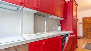 Una cocina con armarios rojos, una encimera blanca y un lavavajillas integrado.