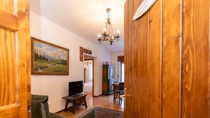 Un salón acogedor con televisor, un sillón verde y un cuadro de un paisaje montañoso.