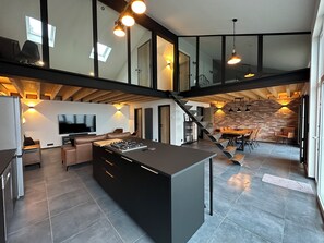 Una cocina amplia con una isla central, un área de comedor con pared de ladrillo y una escalera que conecta dos niveles.