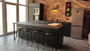 A modern kitchen with a central island, bar stools, a brick wall, a clock, and a refrigerator. - Au 171 Le loft avec un Sauna (Flémalle)