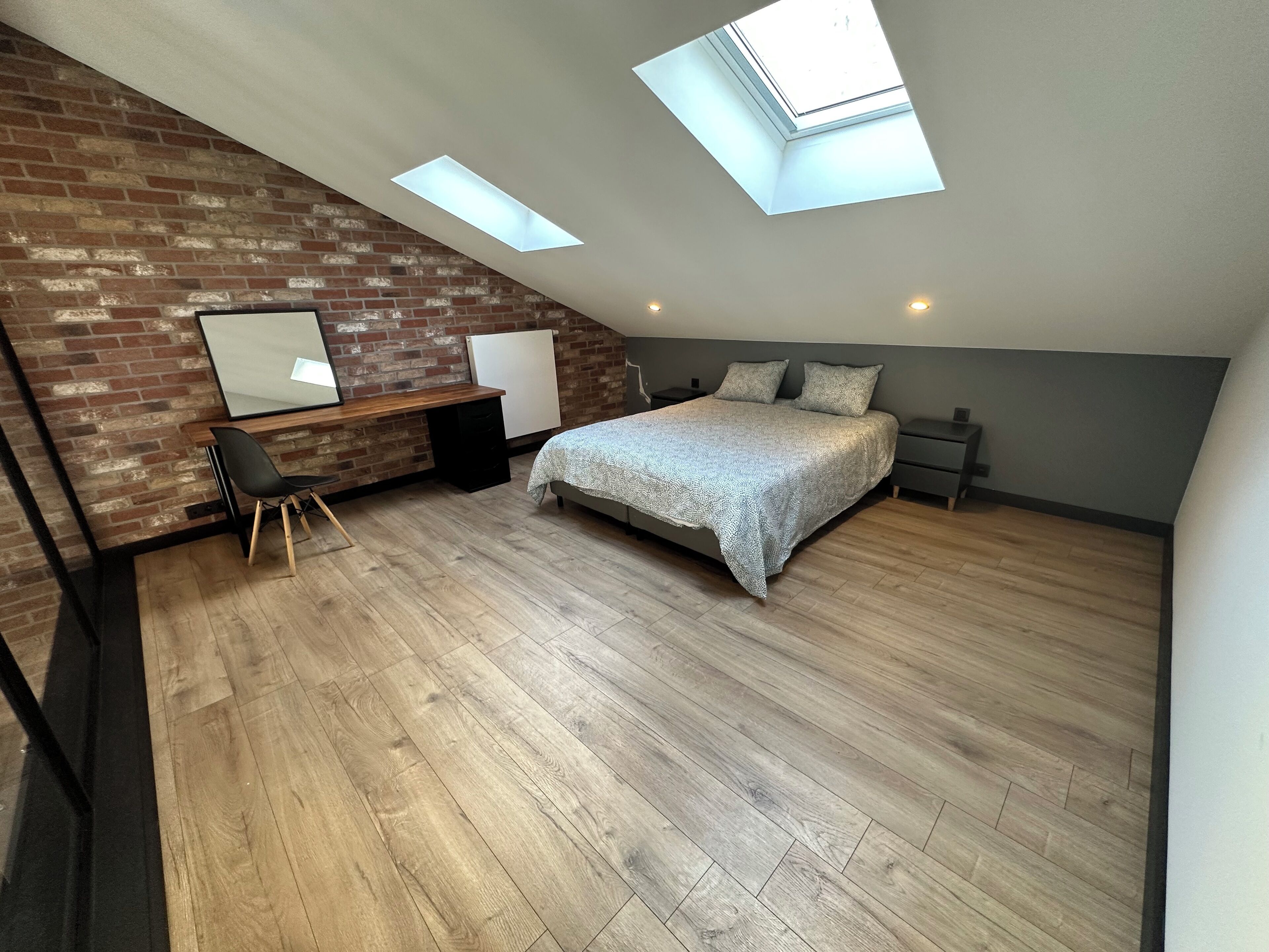 A bedroom with a sloped ceiling, skylights, a bed, a desk, and a chair.