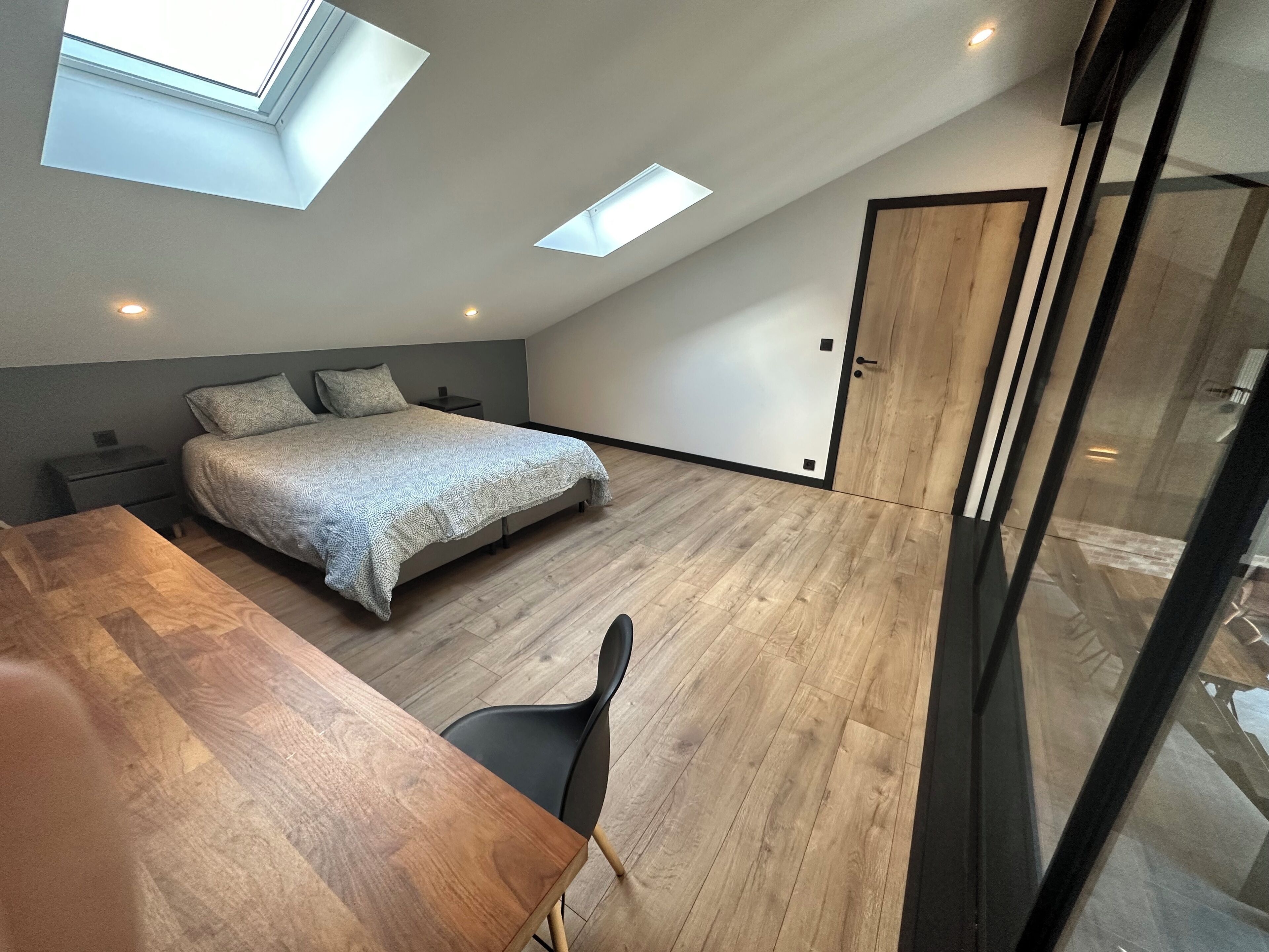 A modern bedroom with a skylight, a bed, a wooden table, and a chair.
