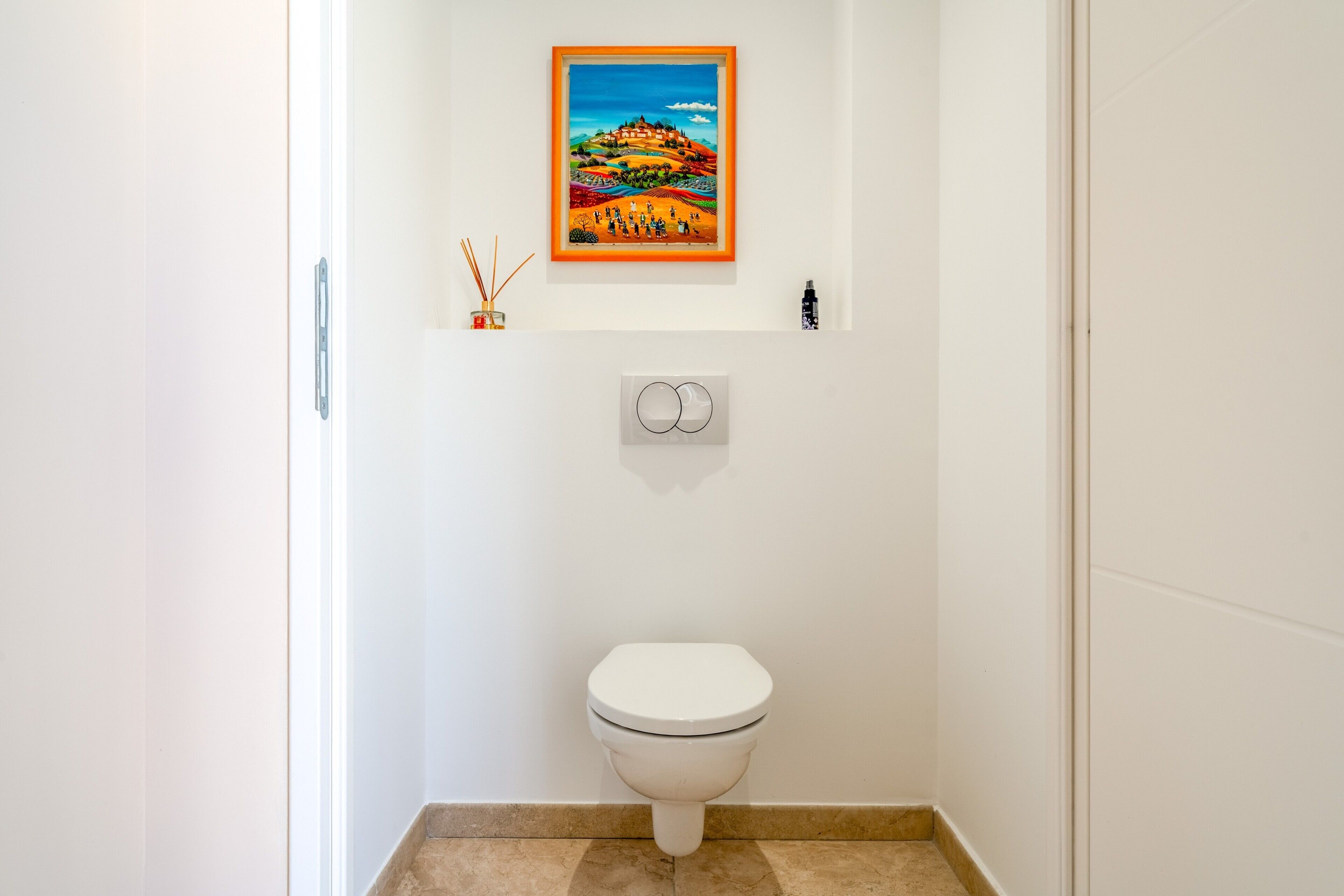 A bathroom with a toilet, a framed painting, and a wall-mounted light switch.