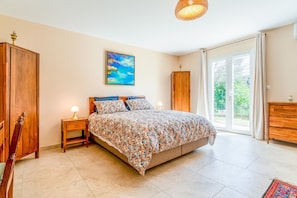 Ein Schlafzimmer mit Bett, Nachttisch, Kommode, einem Gemälde und einem großen Fenster.