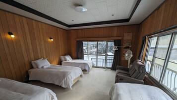 A hotel room with three beds, a sofa, a ceiling fan, and large windows.
