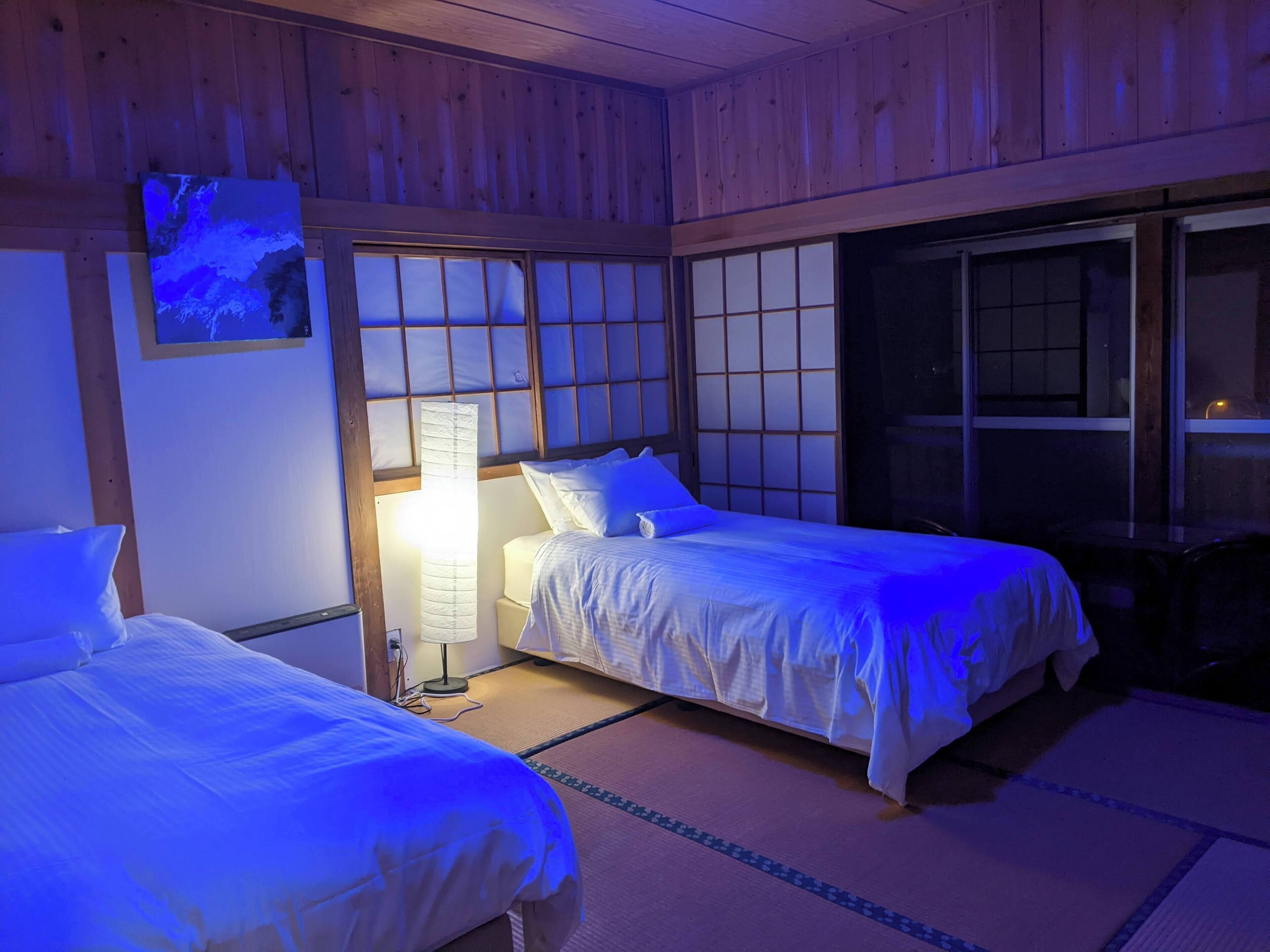 A room with two beds, a nightstand, a lamp, and a window with a view.