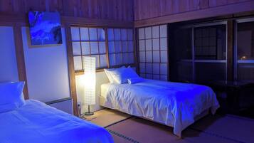 A room with two beds, a nightstand, a lamp, and a window with a view.