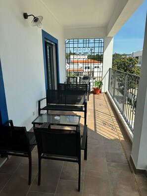A balcony with a table and chairs, a potted plant, and a view of buildings in the background. - Casa do Belé (Faro)