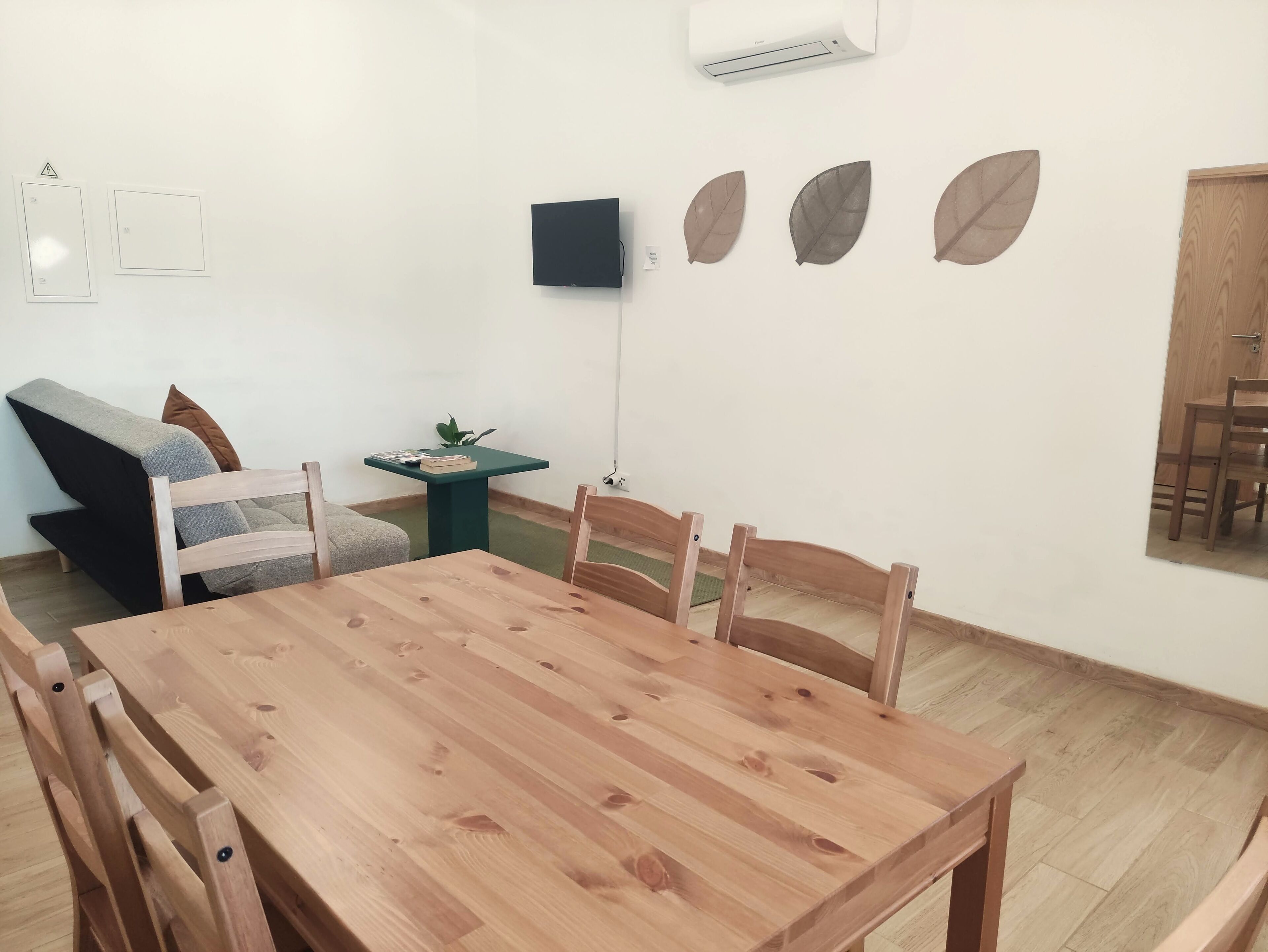 Un coin repas avec une table et des chaises en bois, une petite table d’appoint verte, un canapé et un climatiseur fixé au mur.