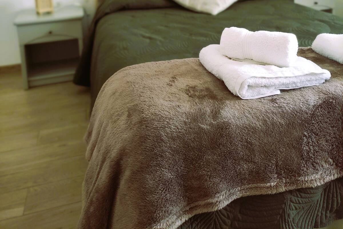 A neatly made bed with a brown blanket and white towels, a wooden headboard, and a wall-mounted decorative leaf.