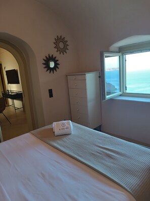 A hotel room with a bed, a wardrobe, a desk with a chair, a sun decoration, and a window with a view of the sea. - Kamari Real Living, with Caldera views and Jacuzzi (Manolas)