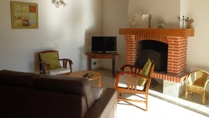 A living room with a brick fireplace, a television, a sofa, and a wicker chair. - Charming house with shared pool in Contres (Contres)