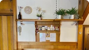 Un banco de madera con asiento acolchado, una mesa de madera y una silla en una habitación con paneles de madera y un tablón de anuncios con papeles y un reloj en la pared.