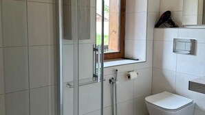 Un baño moderno con cabina de ducha de vidrio, inodoro y lavamanos con ventana superior.