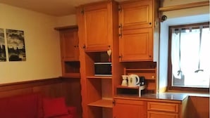 Un espacio habitable compacto con armarios de madera, un sofá rojo y una pequeña cocina con microondas y cafetera.