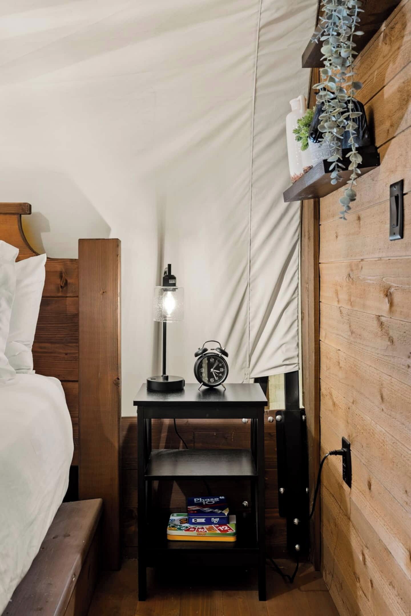 Um quarto aconchegante com cabeceira de madeira, mesa de cabeceira com luminária, relógio e prateleira com livros.