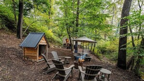 Un área de estar al aire libre rústica con sillas Adirondack, un brasero y una pequeña estructura de madera.