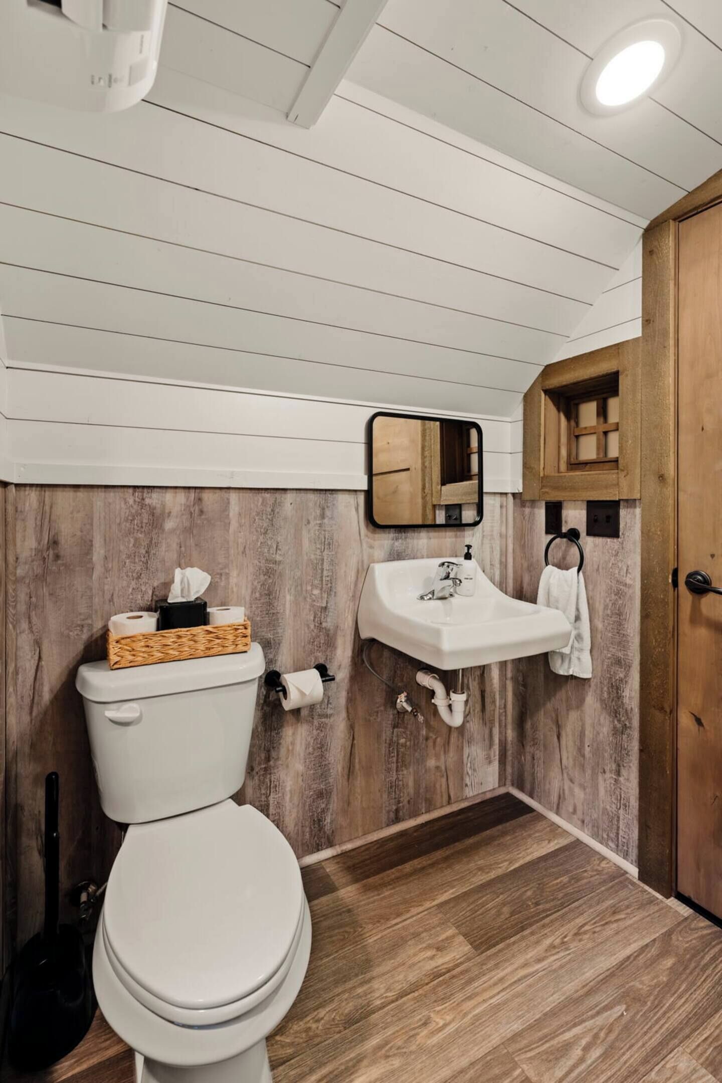 A bathroom with a wooden wall, a white toilet, a sink with a mirror, and a towel rack.