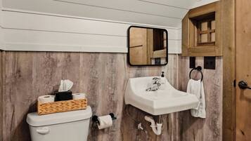 A bathroom with a wooden wall, a white toilet, a sink with a mirror, and a towel rack.