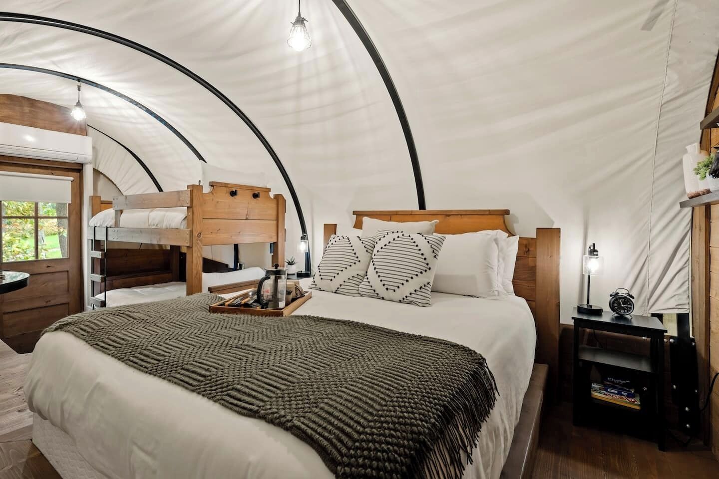 A tented room with a bunk bed, a bedside table with a lamp, and a small shelf.