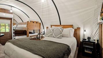 A tented room with a bunk bed, a bedside table with a lamp, and a small shelf.