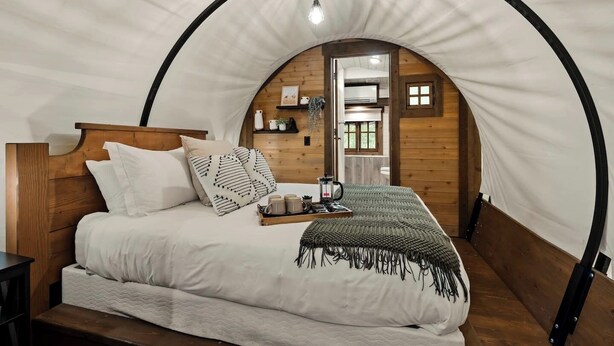 Un dormitorio acogedor de estilo arquitectónico con arco, con cabecera de madera, cama con ropa de cama blanca, mesita de noche y lámpara colgante.