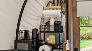 Cocina compacta equipada con microondas, tostadora, cafetera y un estante con artículos básicos de cocina.