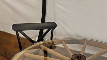 A round glass table with a wooden base and a black metal chair.