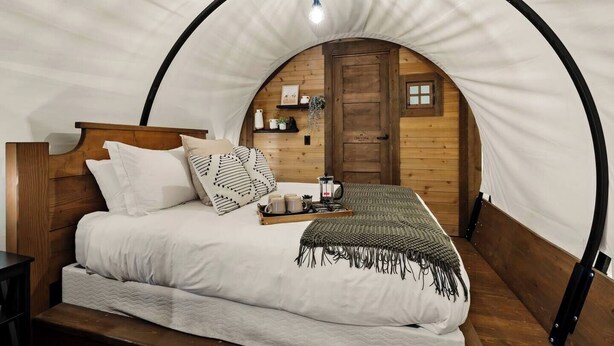 A cozy, arched tent-style bedroom with a wooden bed, pillows, a tray with mugs, and a hanging light fixture.