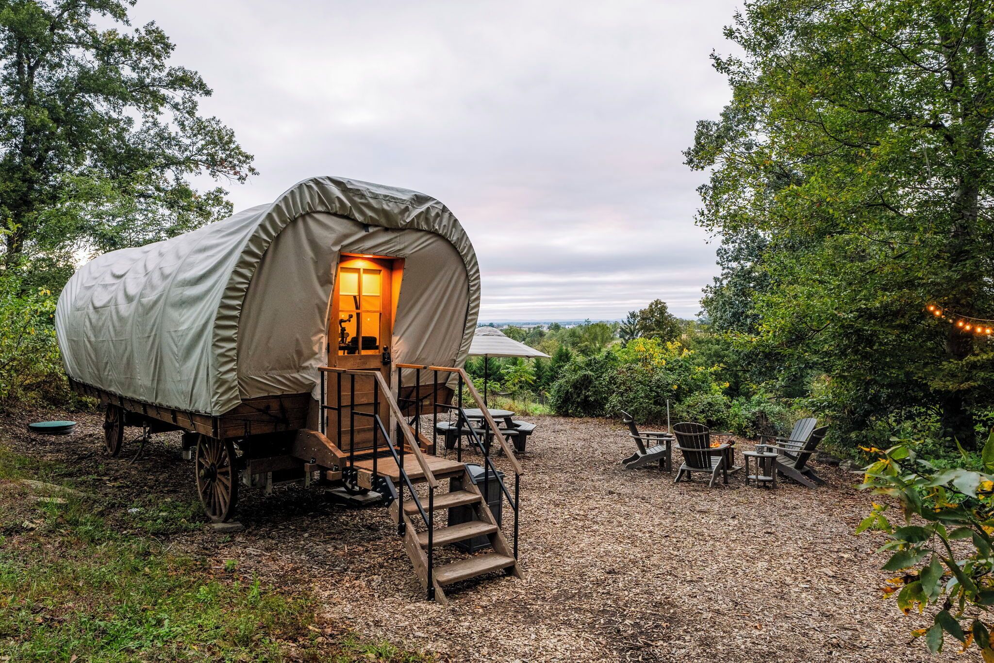 A covered wagon-style tent with a staircase leading to an interior, surrounded by outdoor seating and a fire pit.