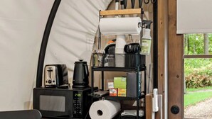 Pequeña cocina equipada con microondas, tostadora, cafetera y un estante con utensilios de cocina.
