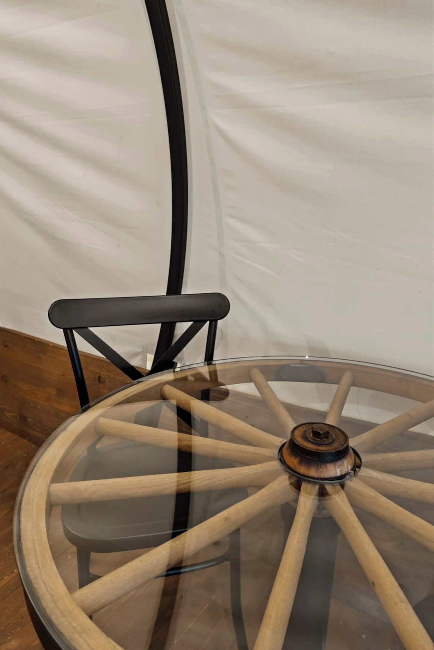 Une table ronde en verre, avec un pied en bois et une chaise en métal noir.