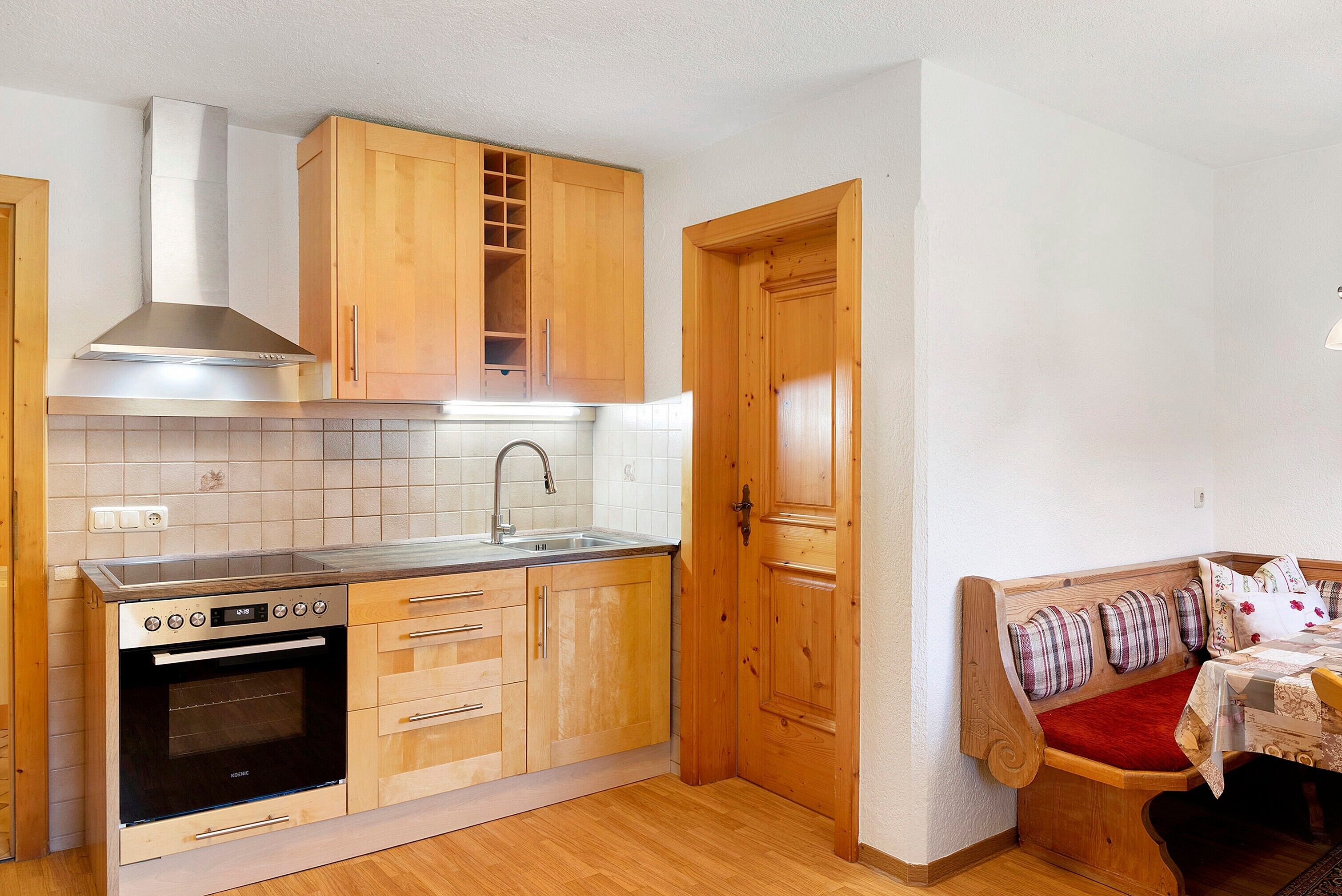 A compact kitchen with wooden cabinets, a stainless steel range hood, a built-in oven, and a sink.