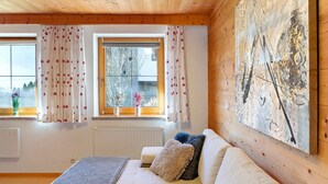 Una habitació acollidora amb sostre de fusta, un sofà blanc amb coixins esponjosos, un quadre abstracte gran i una finestra amb cortines florals.