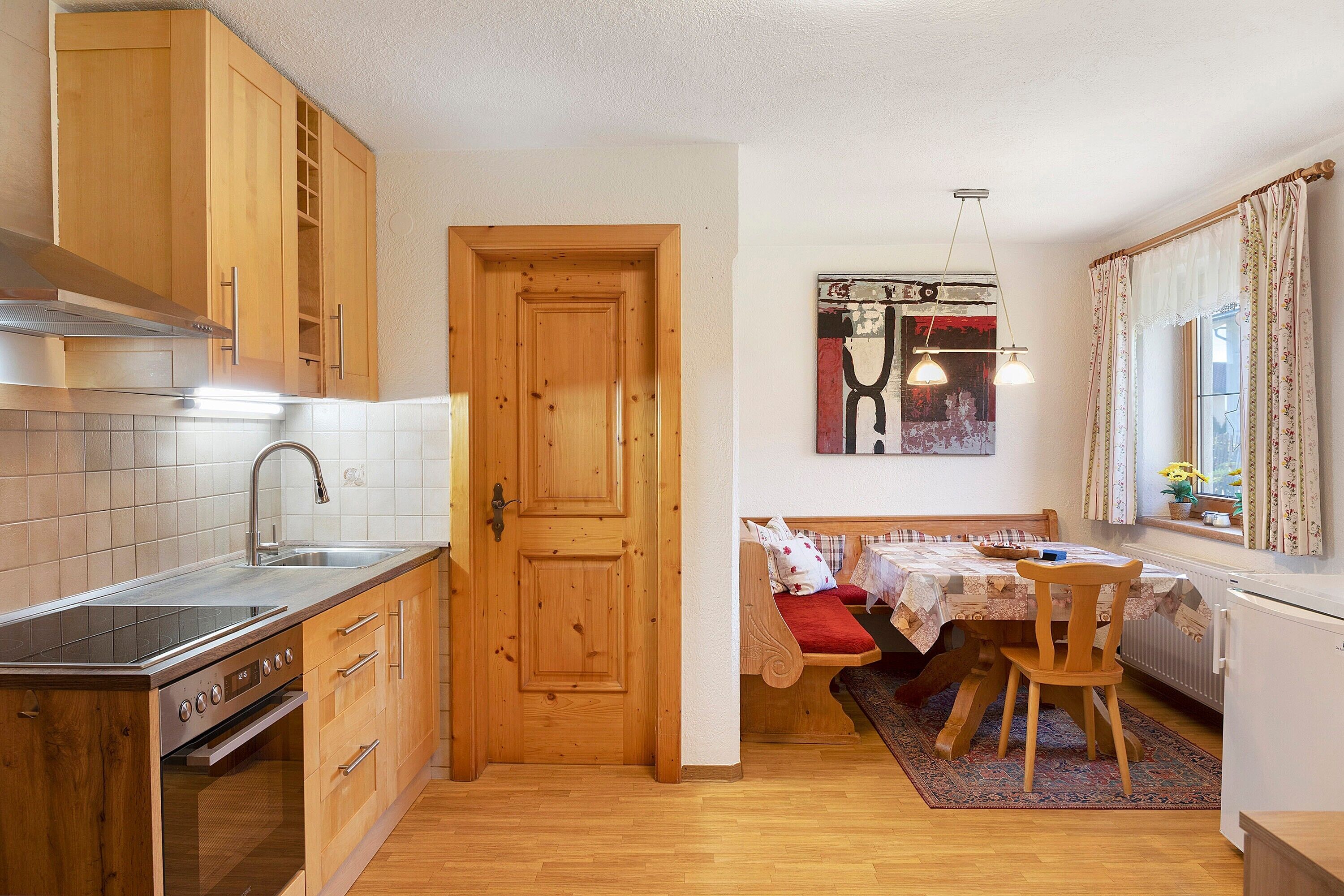 A compact kitchen with wooden cabinets, a built-in stove, and a dining area with a bench and table.