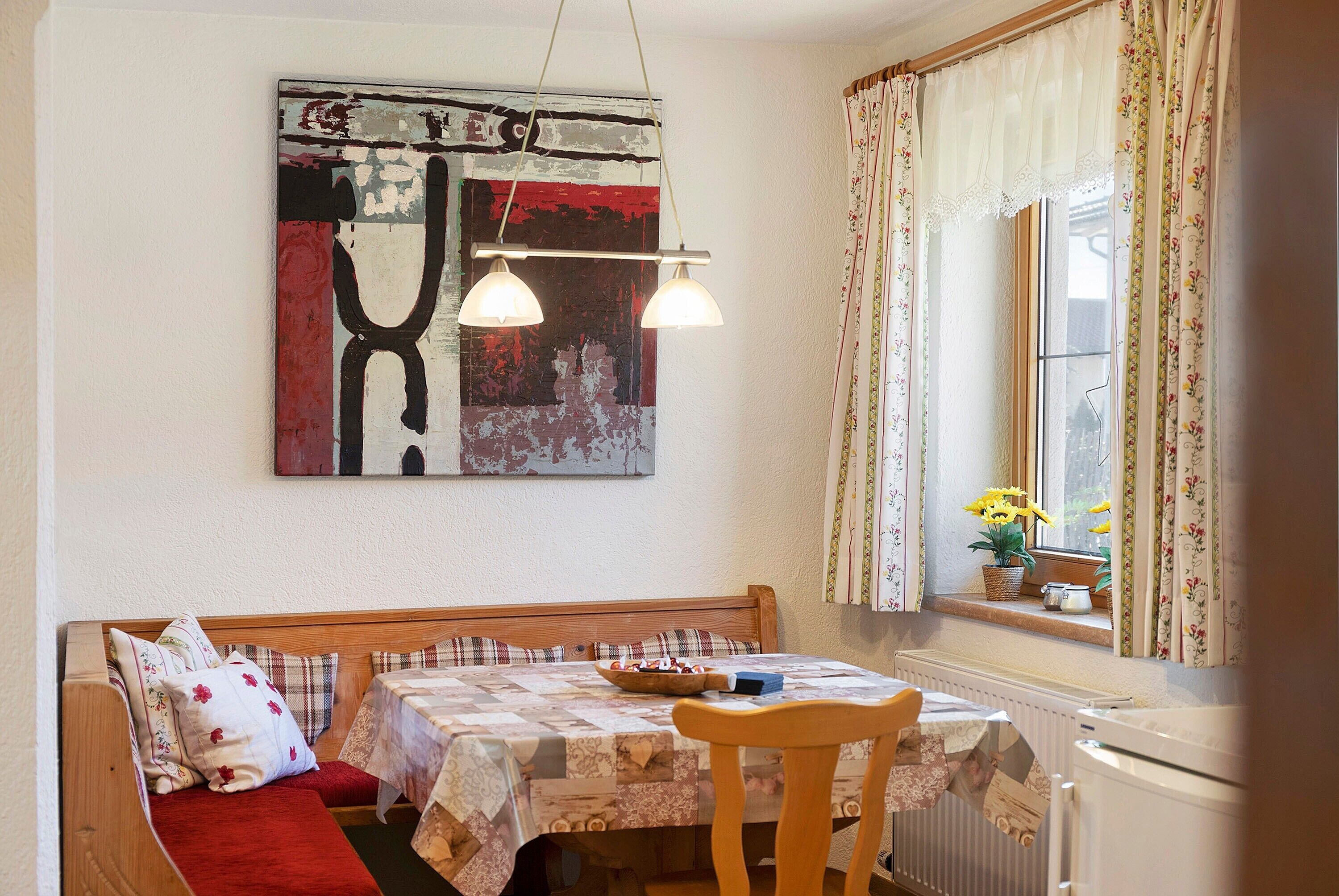 Een eetgedeelte met een tafel gedekt voor twee personen, een bank en een raam met gordijnen.