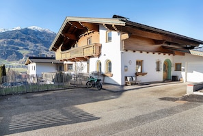 A traditional Alpine-style building with a balcony, a gravel driveway, and a mountain backdrop.