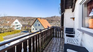 A balcony with a wooden railing, a white bench, and a view of a town with houses and a hill in the background. - Apartment "Sonnenblick" with Balcony and Wi-Fi (Albstadt)