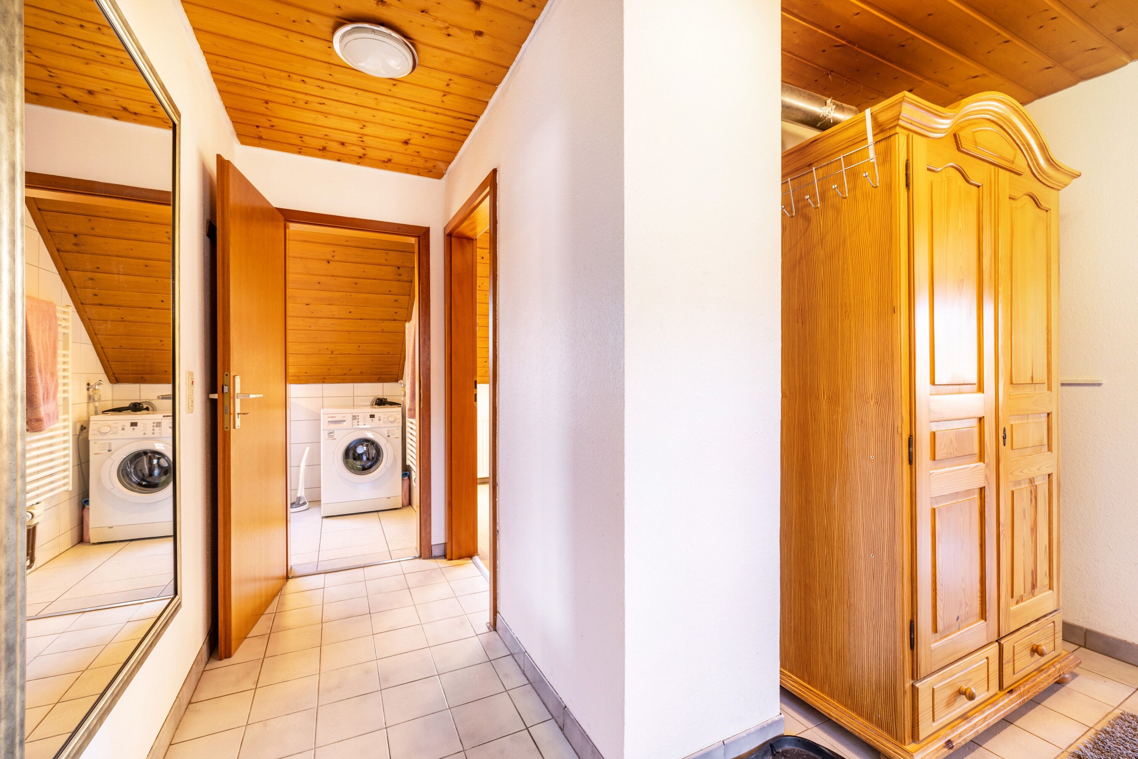A hallway with a wooden ceiling, a washing machine, and a wooden wardrobe.