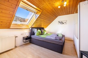 Un dormitorio con techo inclinado, tragaluz, cama con almohadas, mesita de noche con lámpara y radiador.