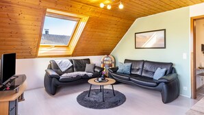 A loft-style room with a sloped ceiling, a large window, a black leather sofa, a small round table, and a television. - Apartment "Sonnenblick" with Balcony and Wi-Fi (Albstadt)