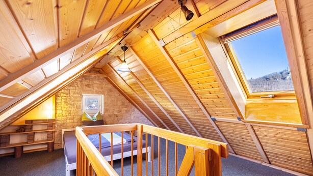 A wooden attic bedroom with a sloped ceiling, a window, a bed, and a small seating area. - Apartment "Sonnenblick" with Balcony and Wi-Fi (Albstadt)