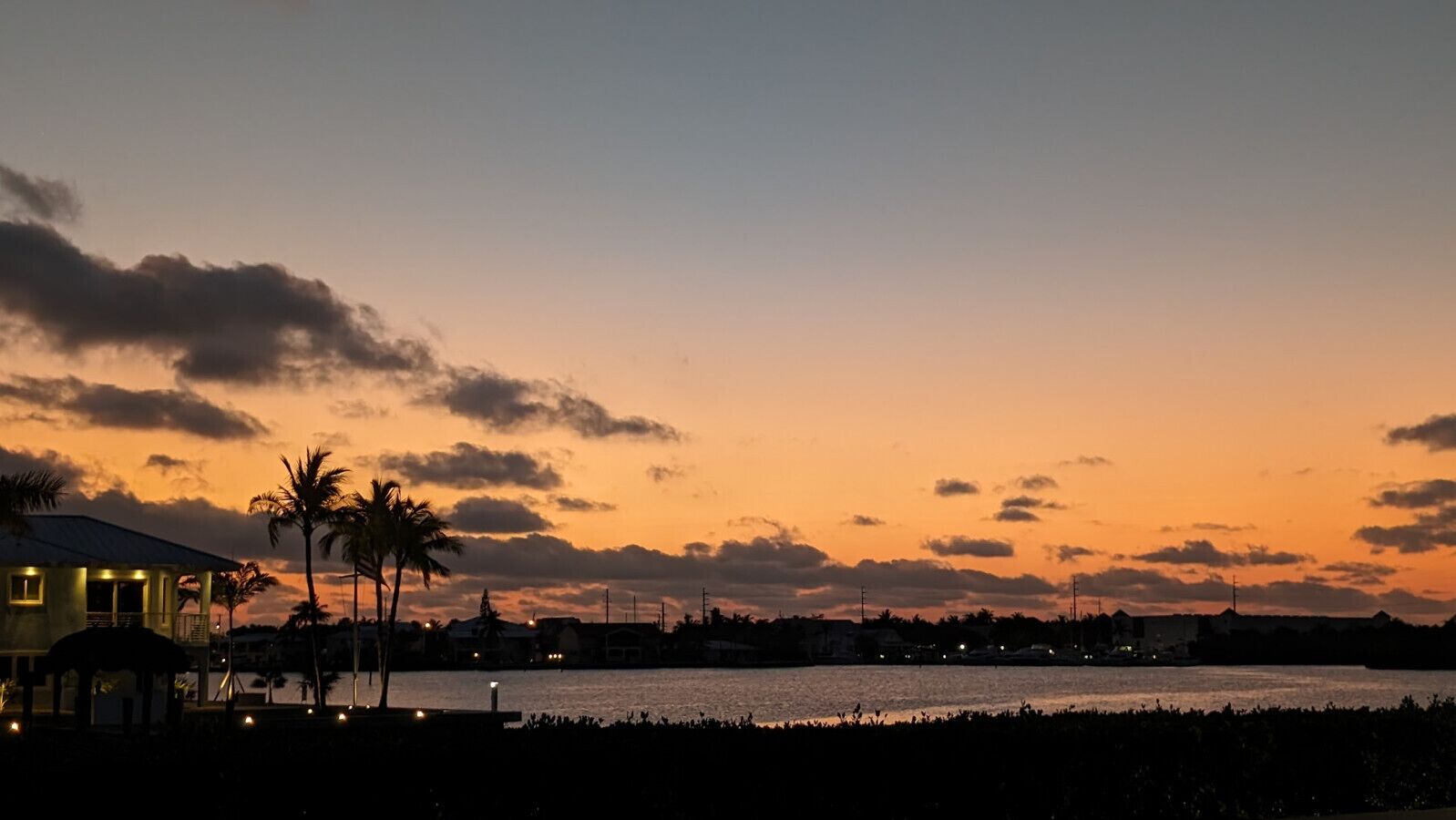 Une vue sur le coucher de soleil en bord de mer, avec un bâtiment et des palmiers.