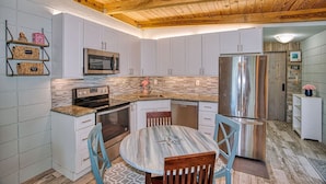 A kitchen with white cabinets, a stainless steel refrigerator, a microwave, and a wooden ceiling. - Keys to the Sea + Cabana Club! (Key Colony Beach)