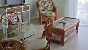 Ein Wohnzimmer mit einem Esstisch aus Glas, Holzstühlen, einem Fernseher und einem Deckenventilator.