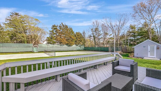 Terraza con mobiliario de mimbre y cancha de tenis.