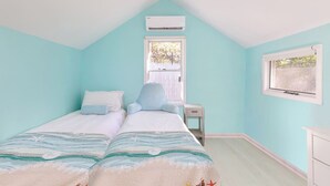 Un dormitorio con dos camas, una ventana, un equipo de aire acondicionado y una mesita de noche pequeña.