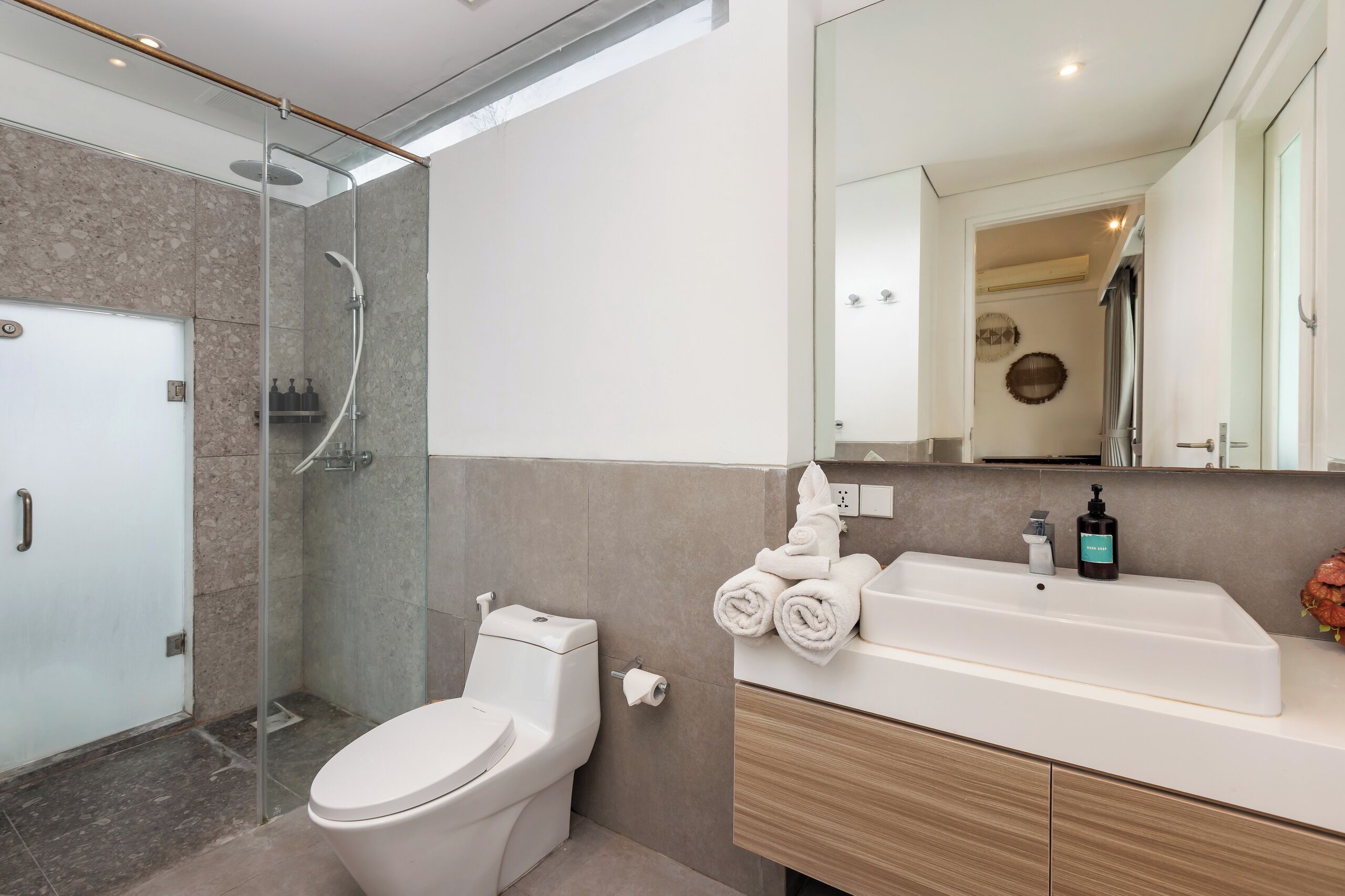 Ein modernes Badezimmer mit einer gläsernen Duschkabine, einer weißen Toilette und einem Waschtisch mit Spüle und Handtuchhalter.