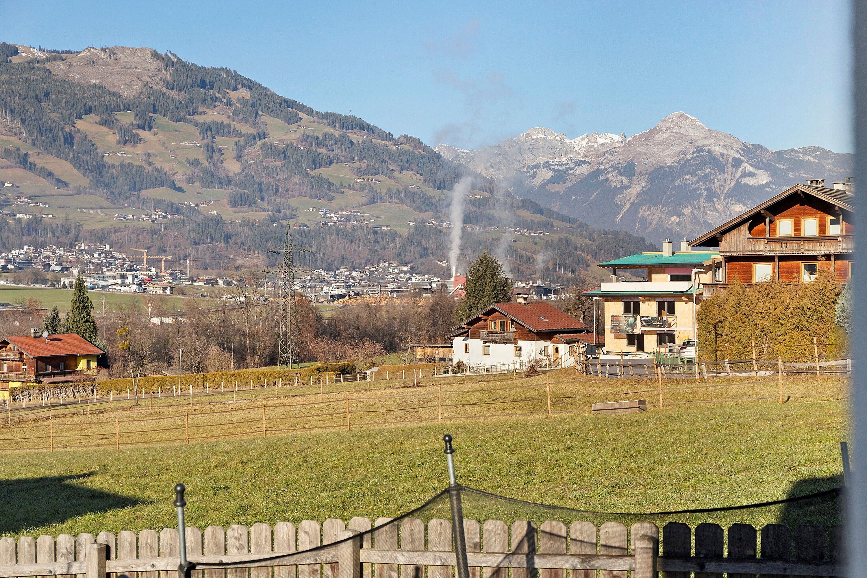 Ein ländliches Dorf mit Bergblick, Holzhäusern und einem eingezäunten Feld.