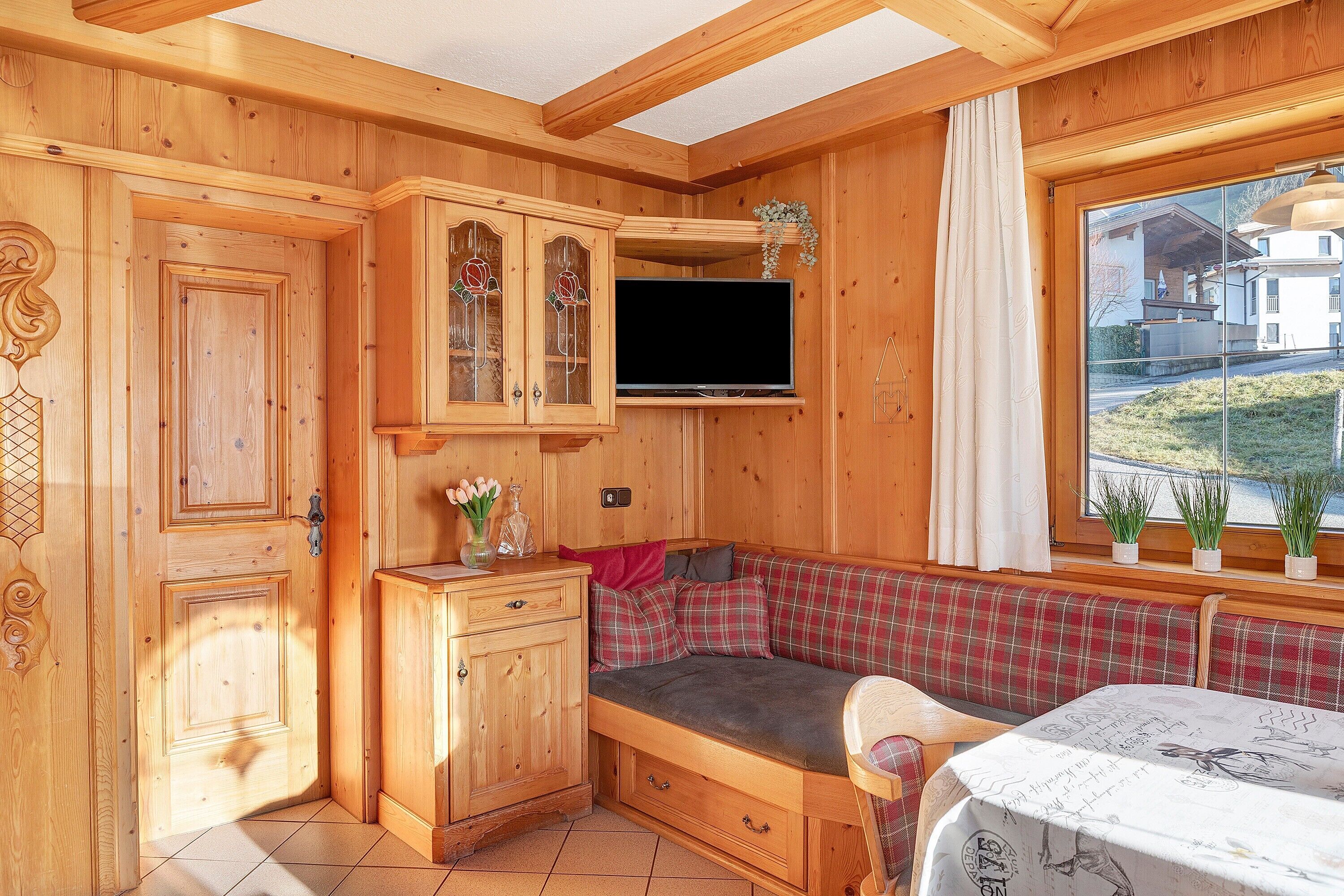 A wooden cabin interior with a television, a bench, and a window with plants.